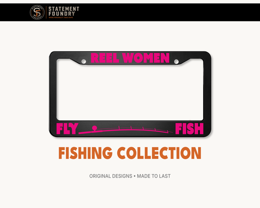 Black metal license plate frame featuring “Reel Women Fly Fish” in bold pink lettering with a fly-fishing graphic.